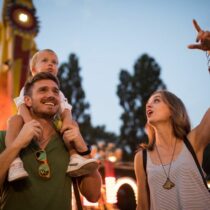 Family with one child outdoors on summer festival. Father carrying son on shoulders, they enjoy in festival entertaining